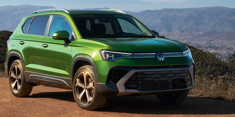 Metallic green Volkswagen Taos SUV parked on a dirt road with mountains in the background.