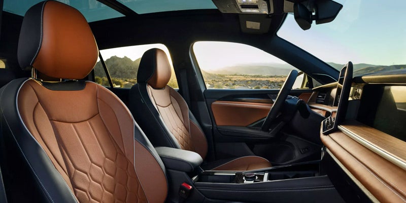 Car interior with tan leather seats and wood trim, viewed from the back right, showing dashboard and desert landscape out the window.
